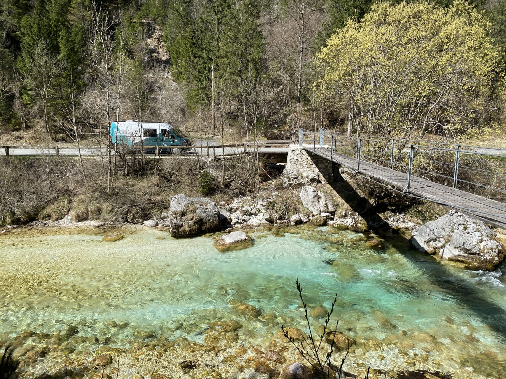 The Electric Campervan is parked up by a cyrstal-clear river in Slovenia next to a suspension bridge