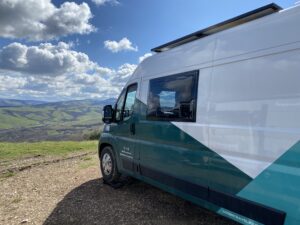 An electric Fiat E-Ducato camper with solar panels parked in Tuscany overlooking fields in sunny weather